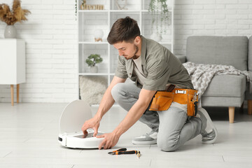 Young man with tool belt fixing modern robot vacuum cleaner at home