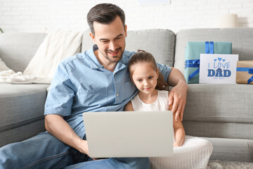 Fathers and his little daughter using laptop in living room. Father's Day celebration