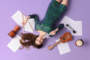 Young female musician with microphone, instruments and music sheets on lilac background