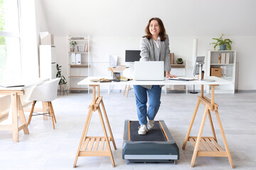 Beautiful businesswoman working with laptop on treadmill at table in office