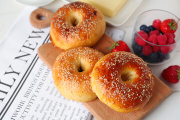 Board with tasty bagels and berries on white wooden background