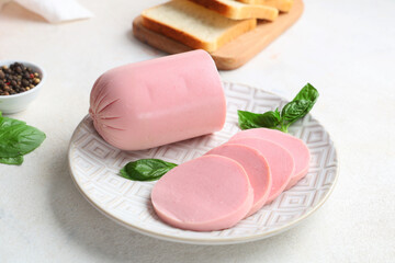 Plate with tasty boiled sausage, basil and slices of bread on grunge white background