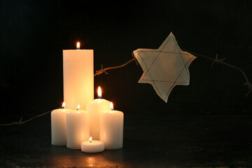 Burning candles with barbed wire and Jewish badge on black background. Day of Remembrance