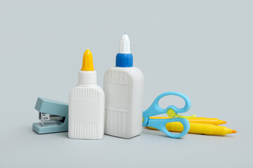 Bottles of glue, scissors and stapler on grey background