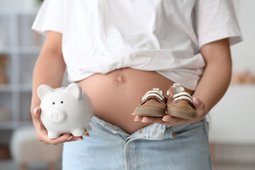 Young pregnant woman with piggy bank and baby booties at home, closeup. Maternal Benefit concept