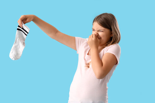 Disgusted little girl with smelly socks on blue background