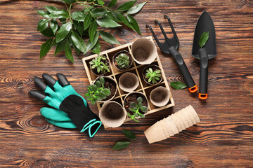 Organizer with plants in peat pots, shovel, gloves and rake on brown wooden background. Gardening...