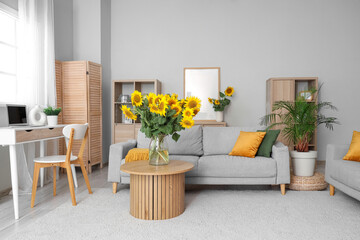 Stylish living room with grey sofa and vases of sunflowers bouquets