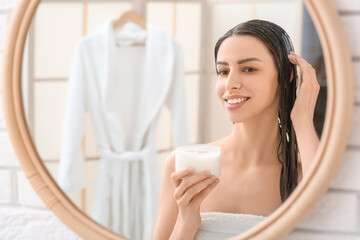 Beautiful young happy woman with jar of hair mask near mirror in bathroom