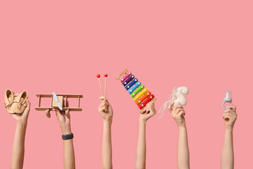 Female hands with baby accessories and toys on pink background