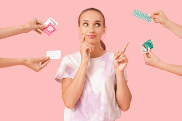 Thoughtful young woman pointing at contraceptives on pink background
