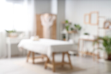 Blurred view of light spa salon with massage couch, shelf units and tables