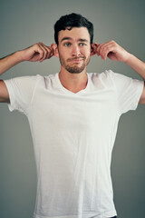 Studio, ear pull and man in tshirt, playful and goofy comedian with gesture for joke in show. Grey background, funny and person with silly facial expression, hands and comic for comedy in USA