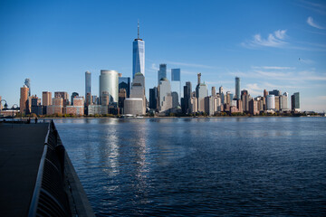 Obraz premium Lower Manhattan and One World Trade Center in New York City, USA as seen from Weehawken New Jersey. Skyscrapers of Manhattan located near rippling water of New York bay against blue sky.