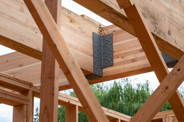 Closeup detail of new house construction, large glue laminate support beams connected by black metal brackets
