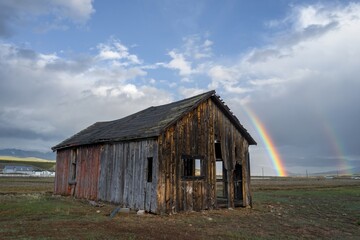 Obraz premium Abandoned wooden barn in the countryside. Behind it is a large rainbow. Leadville, Colorado, United States of America.