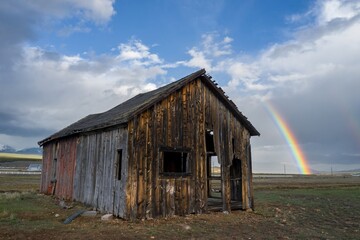 Abandoned wooden barn in the countryside. Behind it is a large rainbow. Leadville, Colorado, United States of America.