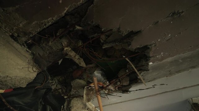 Exposed wires, shattered concrete in Mariupol apartment ceiling after shell hit. Destruction, exposed infrastructure in war impact zone, building interior damage evidences. Slow motion.