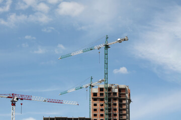 several construction cranes near an unfinished building against blue sky with light clouds