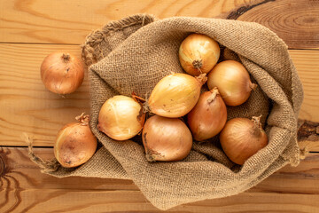 Fresh aromatic onion with jute bag on wooden table, macro, top view.