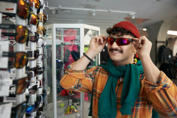 Young hipster man choosing trendy sunglasses at sports shop