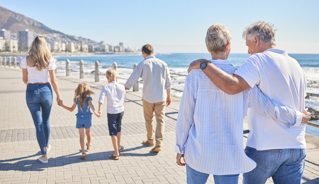 Family, walking and generations for trip to beach, promenade and hug for support in outdoor. Parents, grandparents and children for embrace on vacation, back and holding hands for holiday freedom
