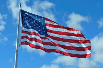 Fototapeta premium An American flag waves against a blue sky with fluffy clouds, symbolizing freedom and national pride under the open sky.