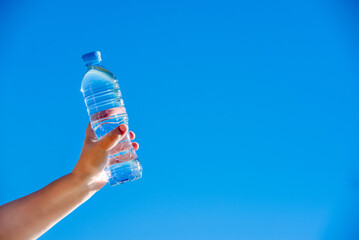 A girl holds a bottle of drinking water in her hand against a blue sky background
