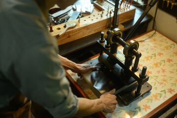 Leather craftsman using a manual rolling machine working on a leather project in his local workshop