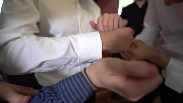 the groom of honor puts the cufflinks on the groom's shirt. detail.