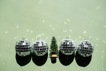 Shiny disco balls and small Christmas tree placed in a row on green background.