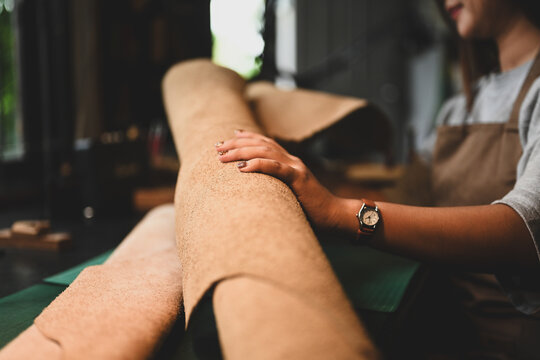 Hand of craftswoman examining a large roll of leather at her workbench surrounded by tools