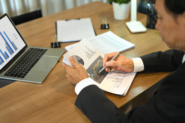 Cropped shot of middle aged businessman examining a financial report at his office desk