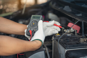 Close-up of mechanic holding voltmeter to check voltage car battery energy problem for service...