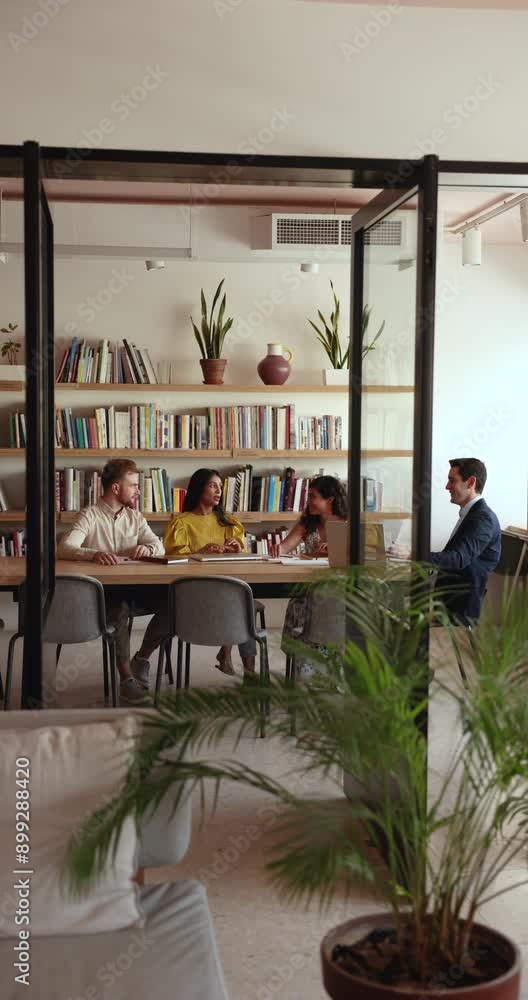 Sticker vertical candid shot of contemporary co-working space with small business team talking at table in b