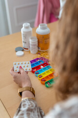 A senior woman organizing the pills she must take during the week and putting them in colored...