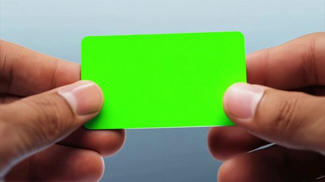 Close up of a business card being held in a man's fingers as he inspect it where the business card is a chroma key green screen.