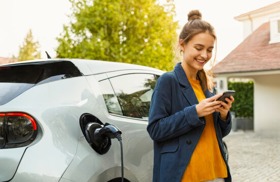 young woman checking vehicle charge level on smartphone. growing trend of sustainable transport, technology in modern life, convenience of monitoring electric car charging status