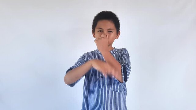 Teenage boy covers his nose with his hand and shows disgust on white isolated background, irritated child with black hairstyle avoids bad smell