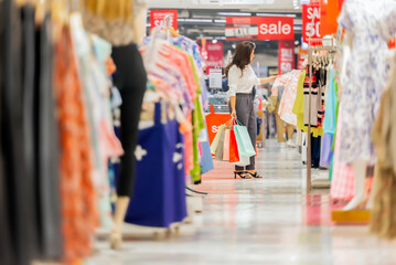 Asian woman holding many shopping bags, feels happy buying new clothes in shopping mall, Choosing stylish clothes, Colorful brand designs. A row of variety clothes hanging on rack. Store discount sign