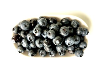 Delicious juicy blueberries isolated on white background. Black blueberries on white saucer. Tasty and healthy food