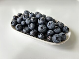 Delicious juicy blueberries isolated on white background. Black blueberries on white saucer. Tasty and healthy food