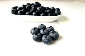 Delicious juicy blueberries isolated on white background. Black blueberries on white saucer. Tasty and healthy food
