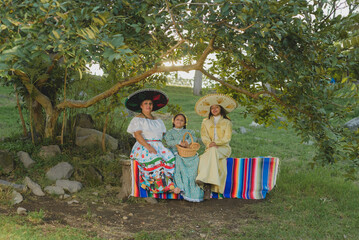 Mother with her daughters wearing typical mexican clothes sitting on sarapes. Rural scenery....