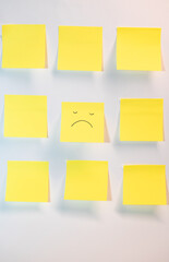 Nine yellow papers and in the center one with a sad face surrounded by eight blank ones.