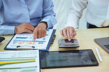 Fototapeta premium Two young Asian businesswomen sit at a table, engaged in a meeting.examine graphs and discuss capital investment strategies, showcasing their expertise and collaborative approach to business growth.