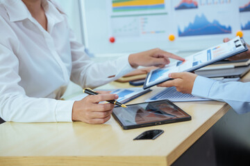 Two young Asian businesswomen sit at a table, engaged in a meeting.examine graphs and discuss capital investment strategies, showcasing their expertise and collaborative approach to business growth.