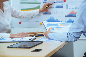 Two young Asian businesswomen sit at a table, engaged in a meeting.examine graphs and discuss capital investment strategies, showcasing their expertise and collaborative approach to business growth.