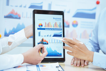 Two young Asian businesswomen sit at a table, engaged in a meeting.examine graphs and discuss capital investment strategies, showcasing their expertise and collaborative approach to business growth.