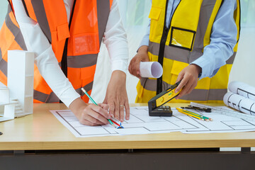 Two young women work at a desk, meticulously designing and drawing plans for building a house. As...